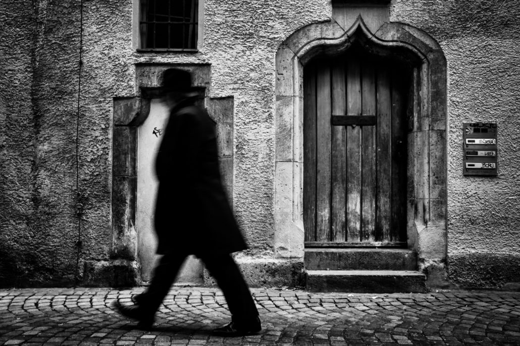 Schwarz-weisse Street-Fotografie eines vorbeigehenden Mannes vor einer Hausfassade.